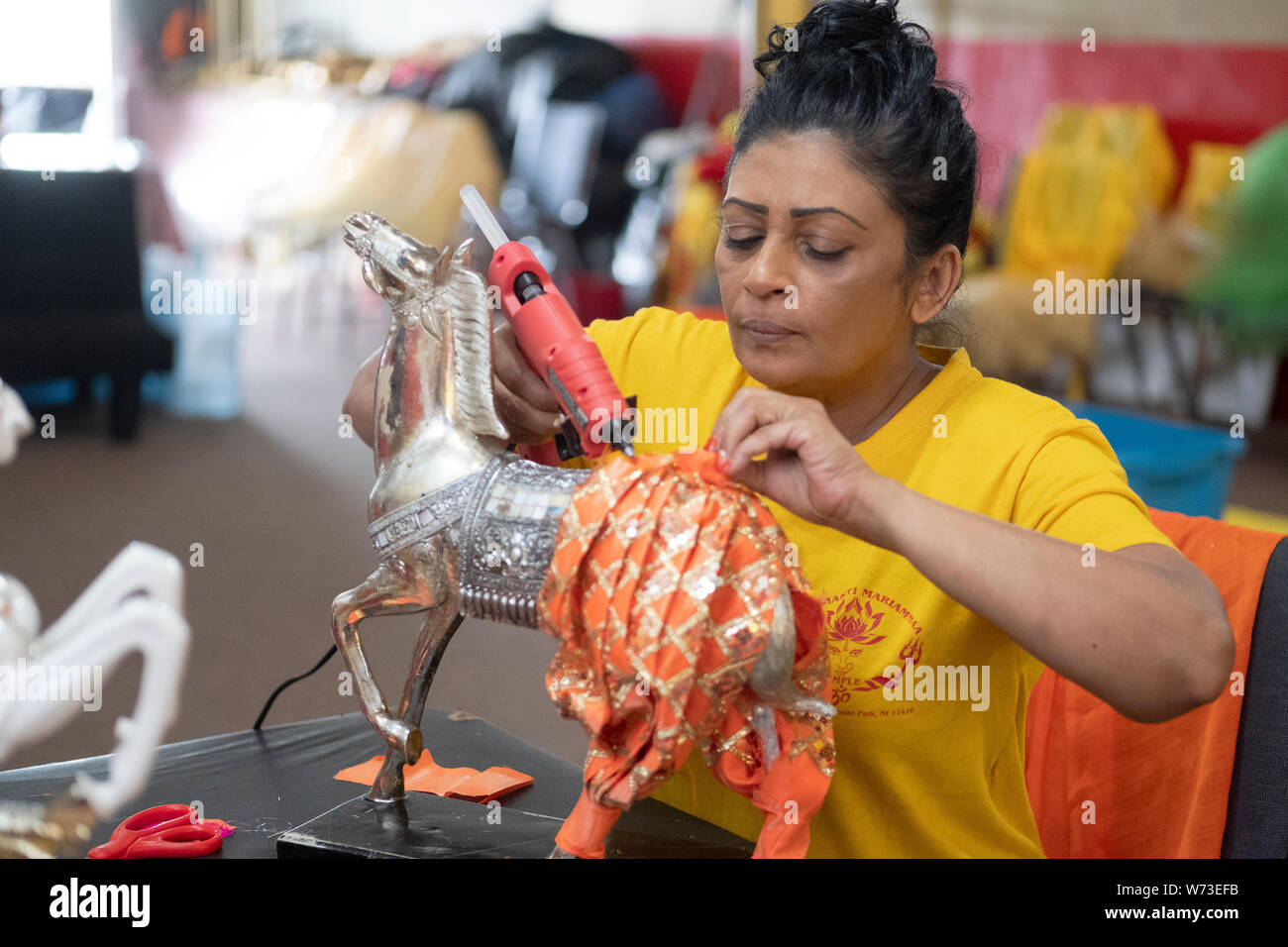 Come parte di un ringraziamento rituale, una pia donna Indù progettato e installato nuovi vestiti sul tempio statue e ornamenti. Nel Queens, a New York. Foto Stock