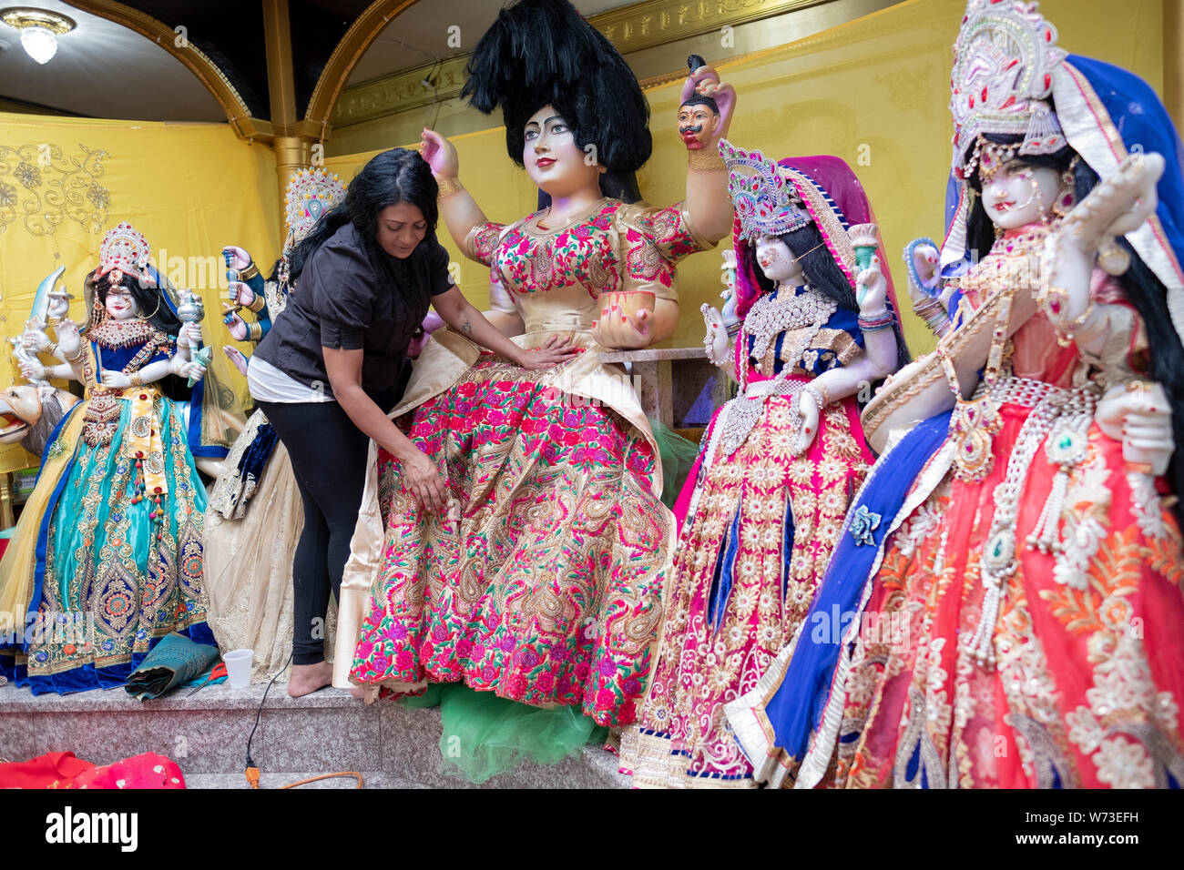 Come parte di un ringraziamento rituale, una pia donna Indù progettato e installato nuovi vestiti sul tempio statue di divinità. In Queens, NYC Foto Stock