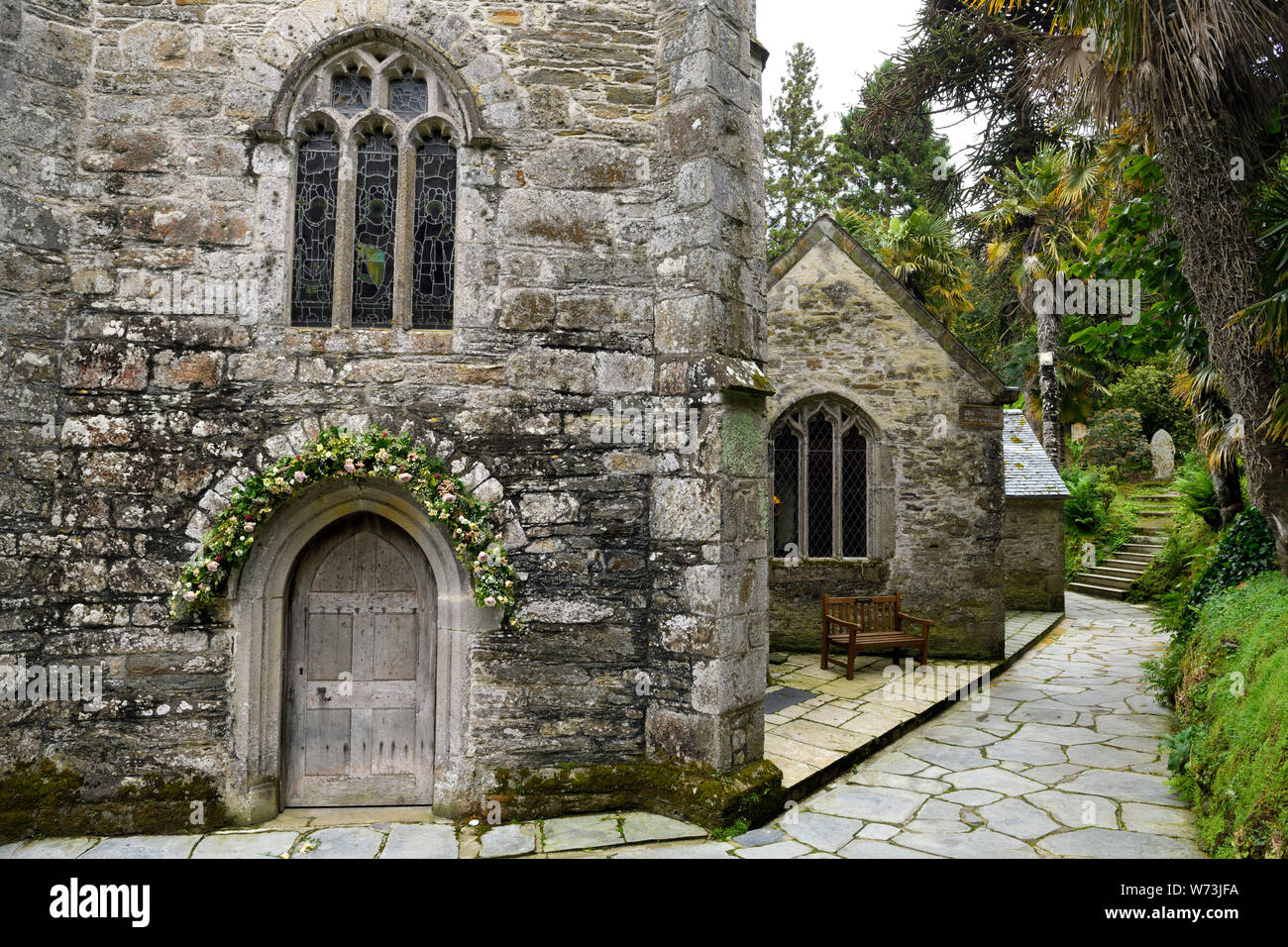 St anglicana appena la chiesa con fiori su porta circondata da palme in San Giusto in Roseland Cornwall Inghilterra con scale per la collina cemet Foto Stock