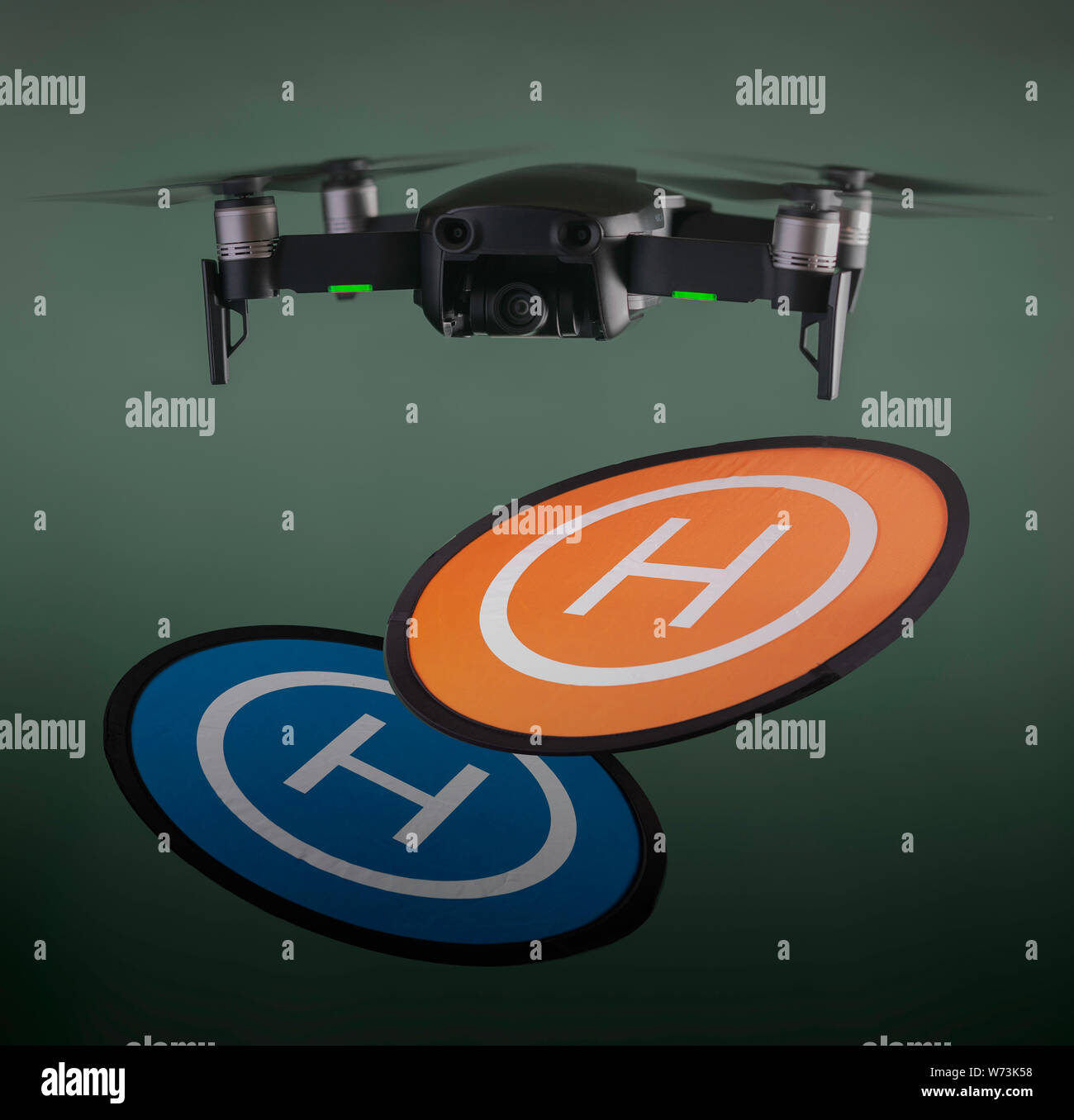 Drone in volo con eliche di filatura e luci di posizionamento in bilico su un arancione e blu di una piazzola di atterraggio contro un verde al di fuori della messa a fuoco lo sfondo Foto Stock