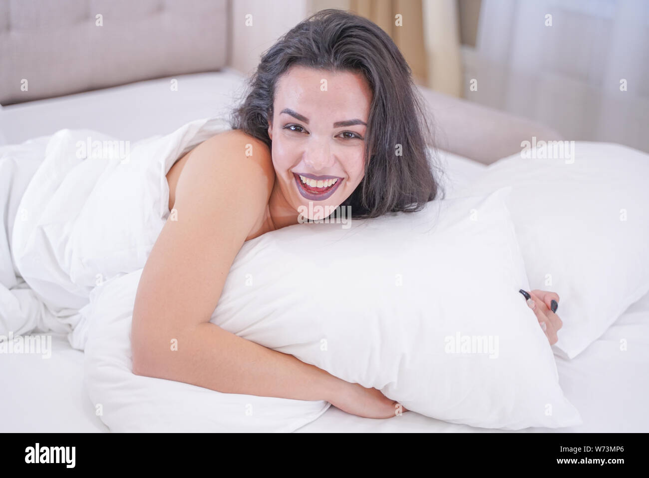 Affascinante bruna giovane ragazza appoggiata nel suo letto bianco Foto Stock