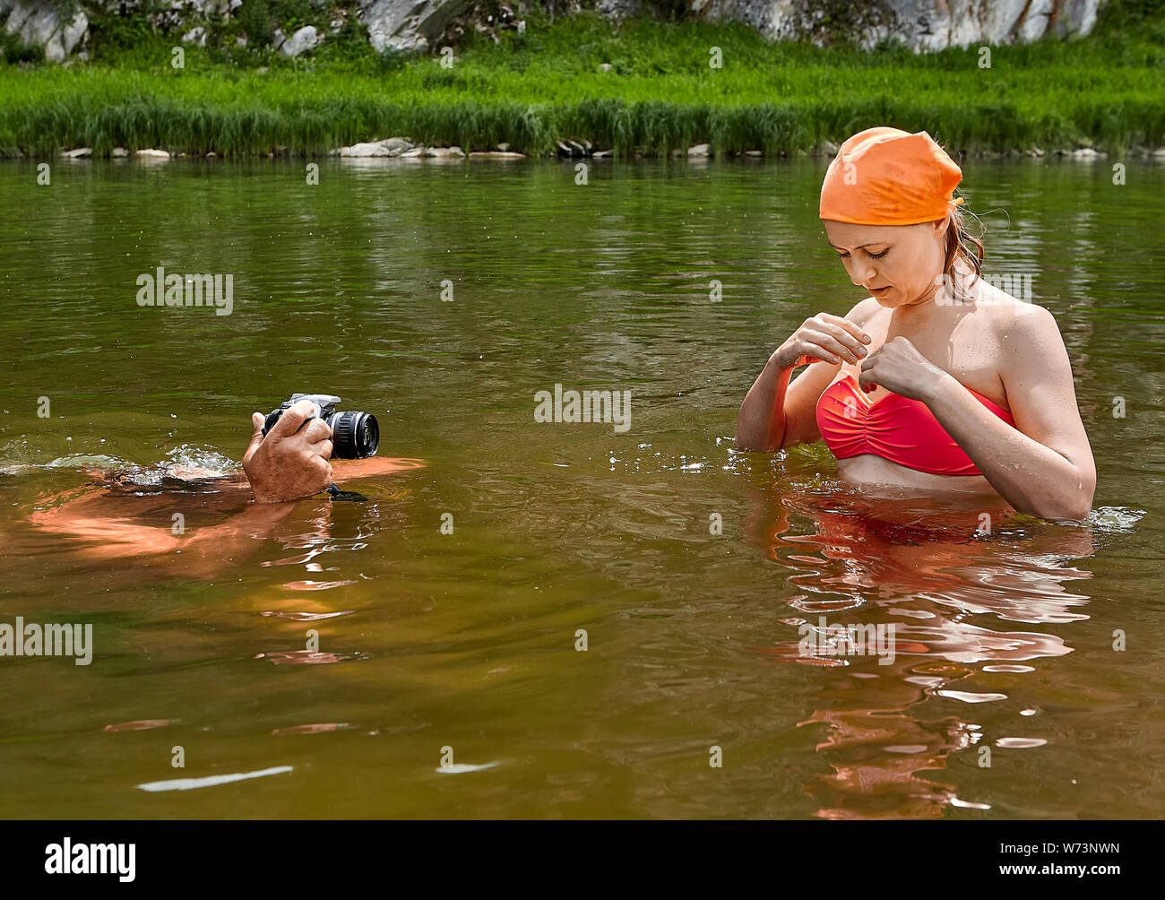 Giovane bella donna in costume da bagno e la bandana arancione è in piedi nel fiume e uomo bianco è scattare foto con il suo nel loro utilizzo macchina fotografica impermeabile. Foto Stock