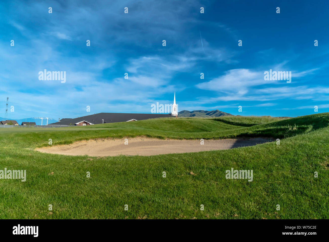 Bunker di sabbia su un campo da golf con vista del campanile e tetti scuri Foto Stock