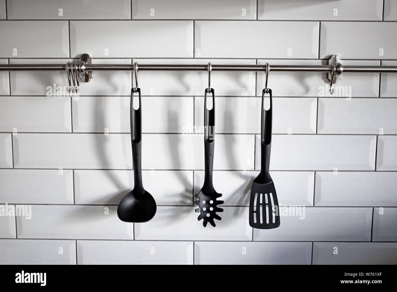 In plastica nera arnese da cucina appendere su bianco muro di pietra. Foto di pentole. Utensili da cucina appeso con mattoni bianchi sfondo. Foto Stock