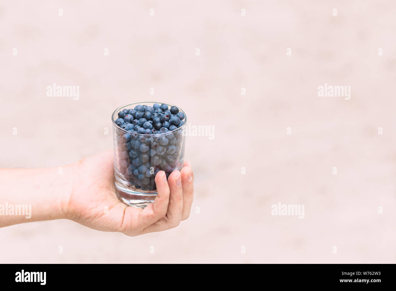 Un bicchiere di mirtilli nelle mani di un ragazzo. Un bicchiere pieno di mirtilli. Spazio per il testo Foto Stock