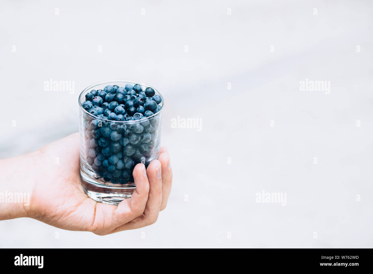 Un bicchiere di mirtilli nelle mani di un ragazzo. Un bicchiere pieno di mirtilli. Spazio per il testo Foto Stock