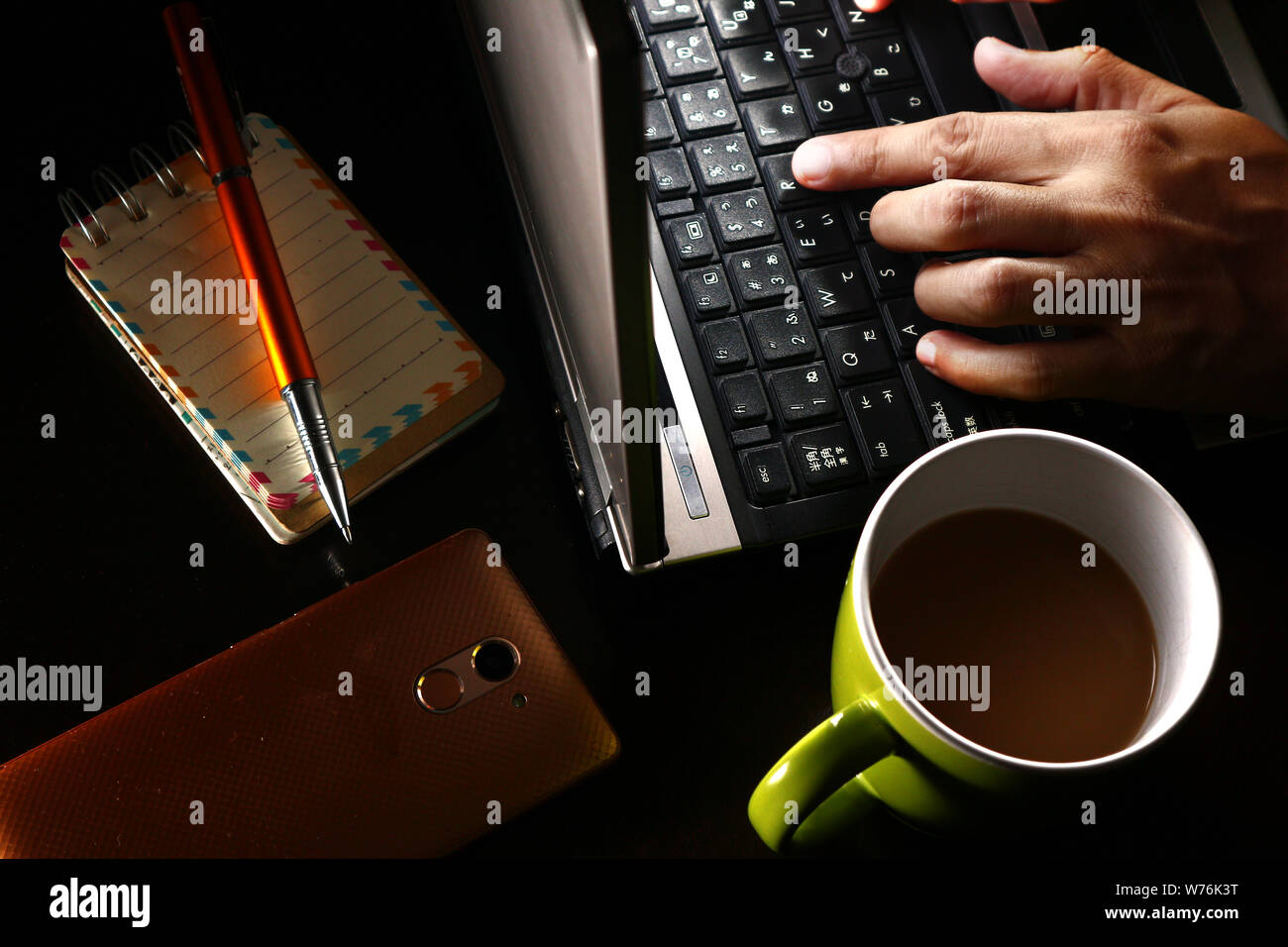 Foto di una mano su un computer portatile, una tazza di caffè, penna a sfera, notebook e uno smartphone Foto Stock