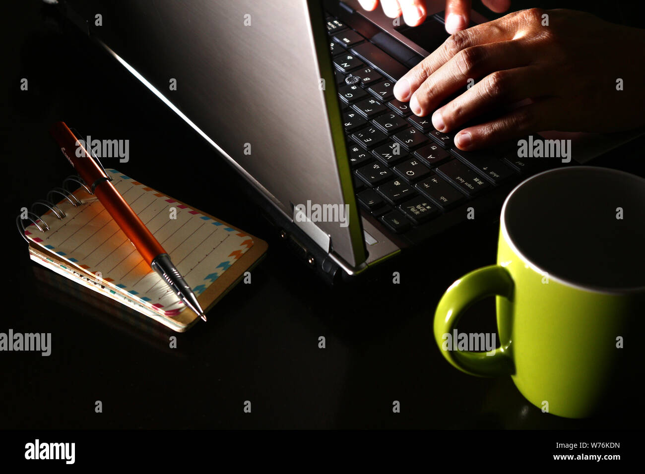 Foto di una mano su un computer portatile, una tazza di caffè, penna a sfera e un notebook Foto Stock