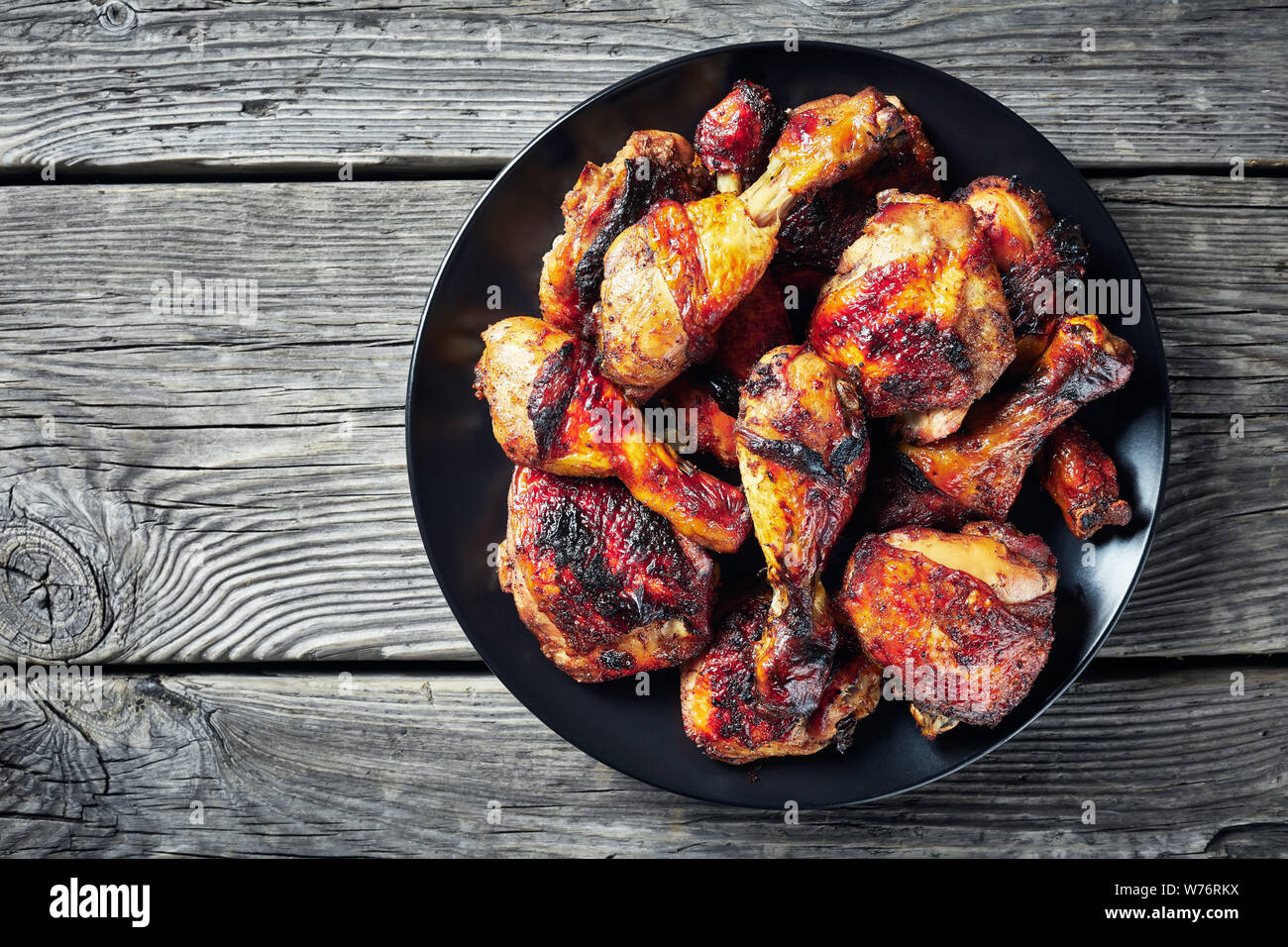 Pollo Jerk su una piastra nera su una tavola in legno rustico, vista orizzontale dal di sopra, close-up, flatlay, spazio di copia Foto Stock