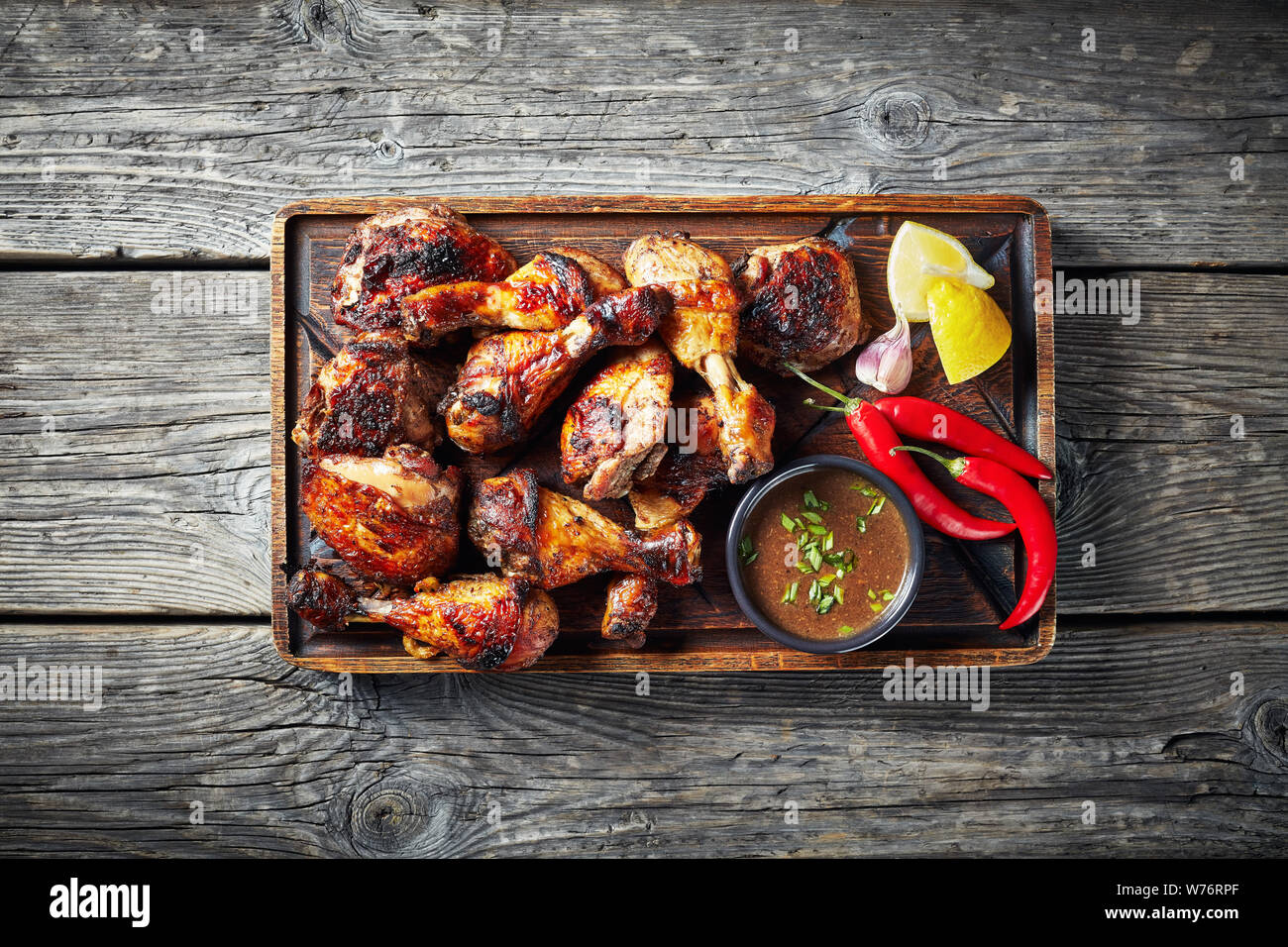Vista aerea del pollo jerk su una scheda di rude con salsa di limone e su una tavola in legno rustico, vista orizzontale dal di sopra, close-up, flatlay Foto Stock