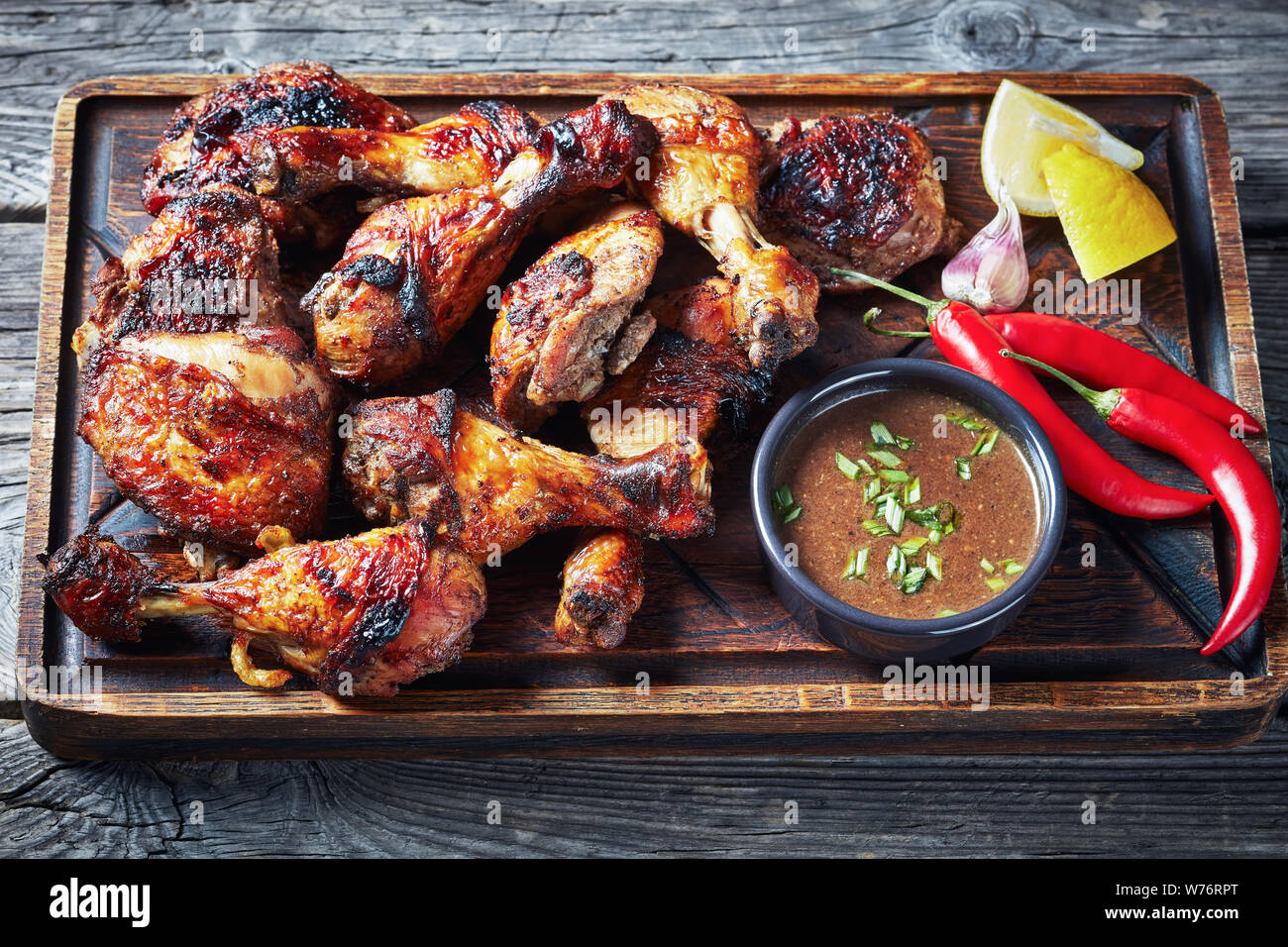 Caldo giamaicano grigliate pollo jerk su una scheda di rude con salsa di limone e su una tavola in legno rustico, vista orizzontale dal di sopra, close-up Foto Stock