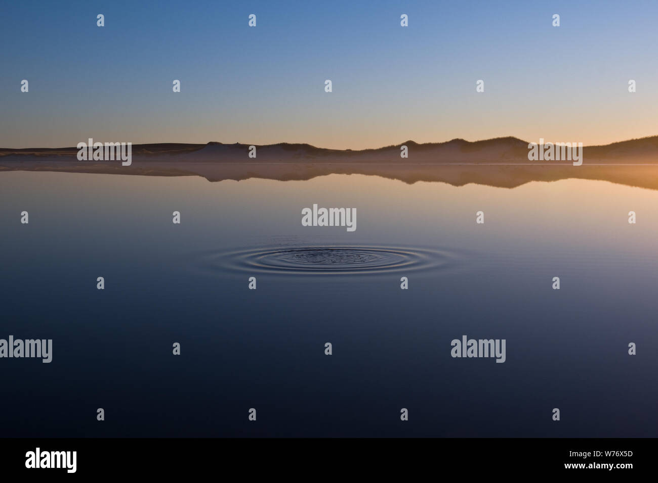 Ripples diffondendo come un Cielo di tramonto riflette in acque calme. Bertha's Beach, East Falkland Foto Stock