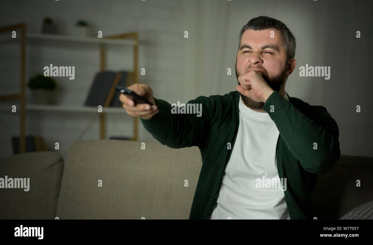 Annoiato uomo canali di commutazione sul TV e sbadigli Foto Stock