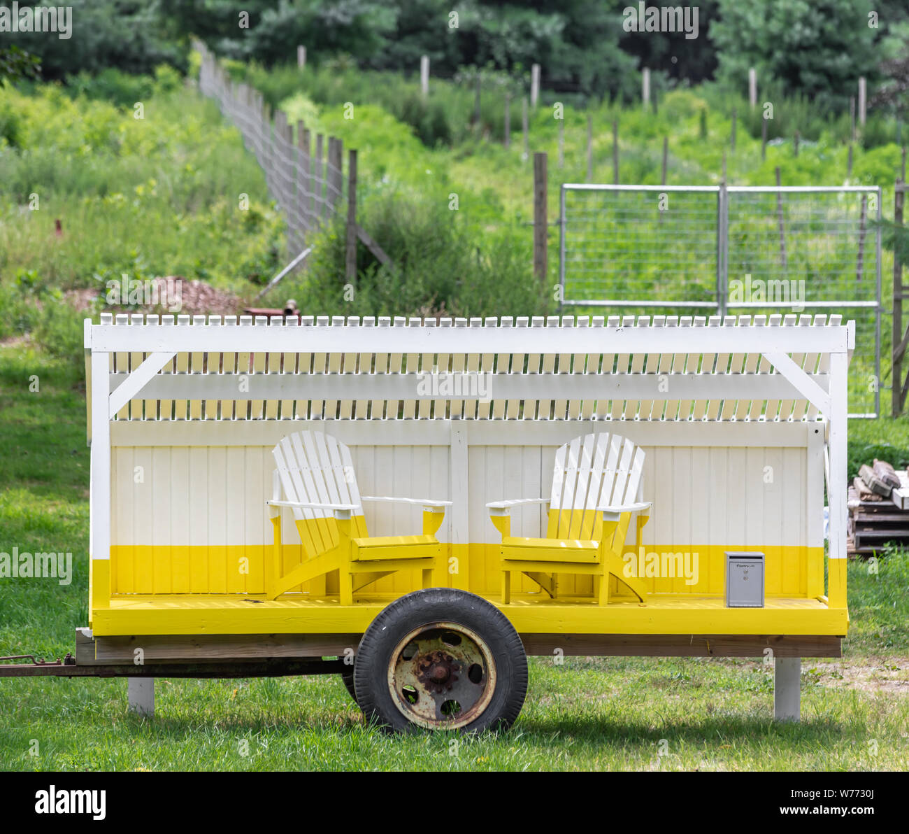 Due di legno porta fuori sedie dipinte di giallo e bianco su un adattamento di giallo e bianco seduta del rimorchio in un paesaggio verde Foto Stock