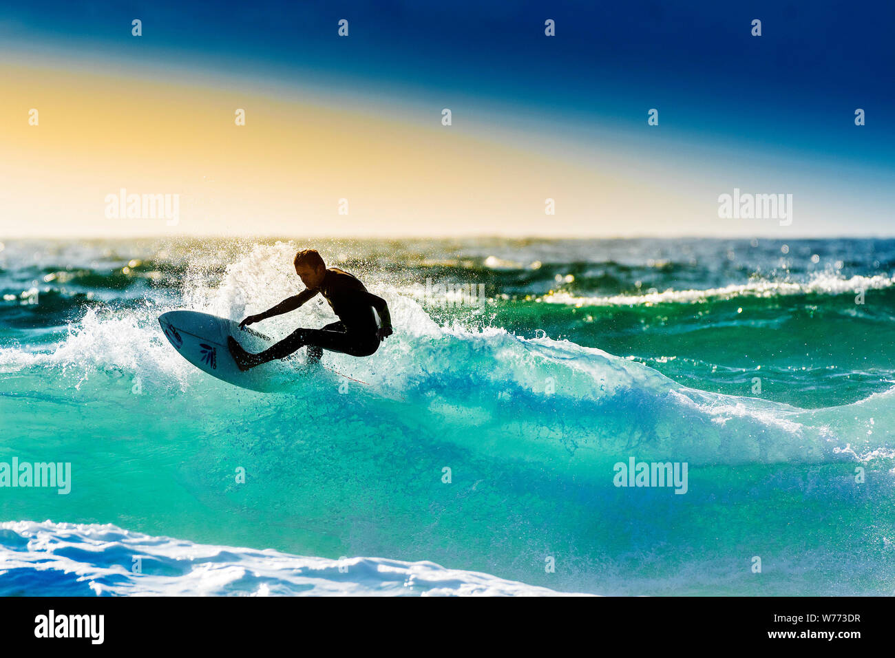 Un surfista cavalcare un onda retroilluminati da sole di setting a Fistral a Newquay in Cornovaglia. Foto Stock