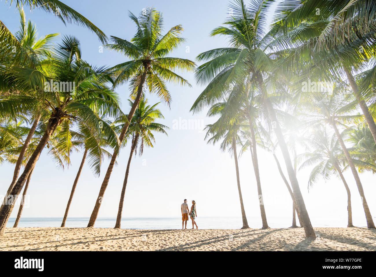 Coppia permanente sulla spiaggia di sabbia tra le palme sulla mattina di sole al mare Foto Stock