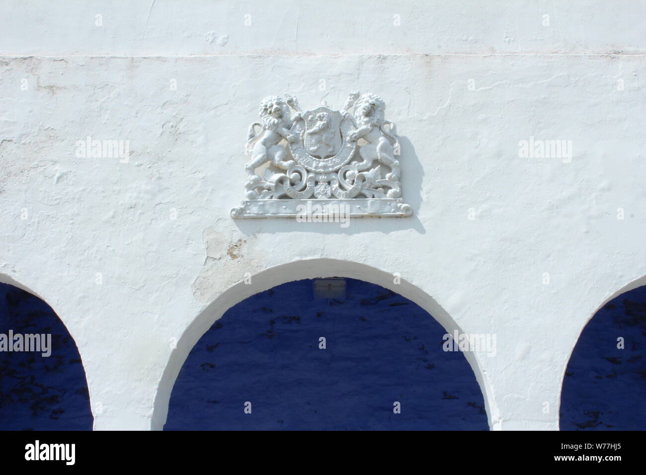 Immagine del muro bianco con Lion che dettaglia, davanti ad un blu scuro sulla parete una giornata di sole in Portmeirion Foto Stock