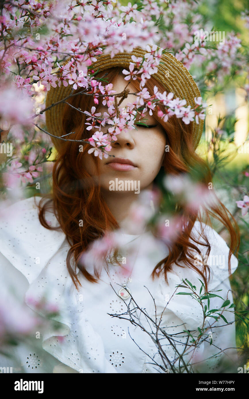 Bellissimi i Capelli rossi ragazza in posa e sognare in primavera fiori di mandorla al tramonto Foto Stock