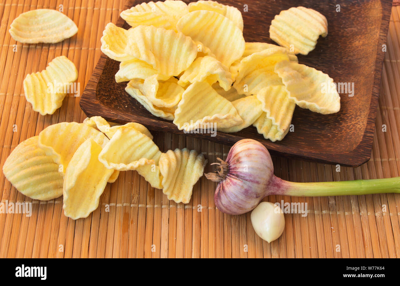 Appetitosi e Croccanti patatine su un tessuto assorbente di bambù in un recipiente di legno, accanto alla testa di aglio, insalubri o cibo sbagliato, ma molto gustosi. Foto Stock