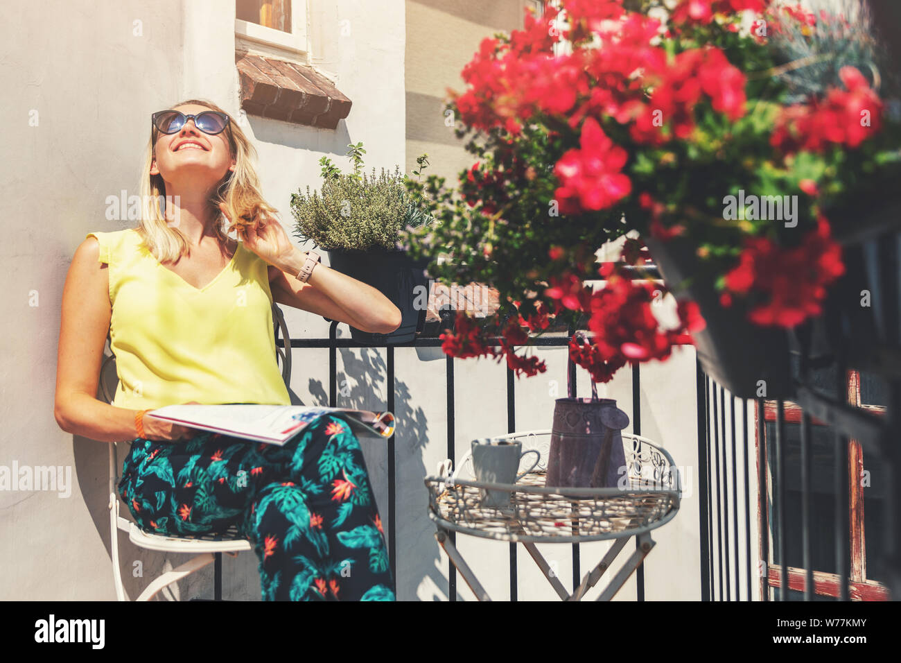 Giovane donna godendo il sole sul romantico balcone con vasi di fiori. Foto Stock