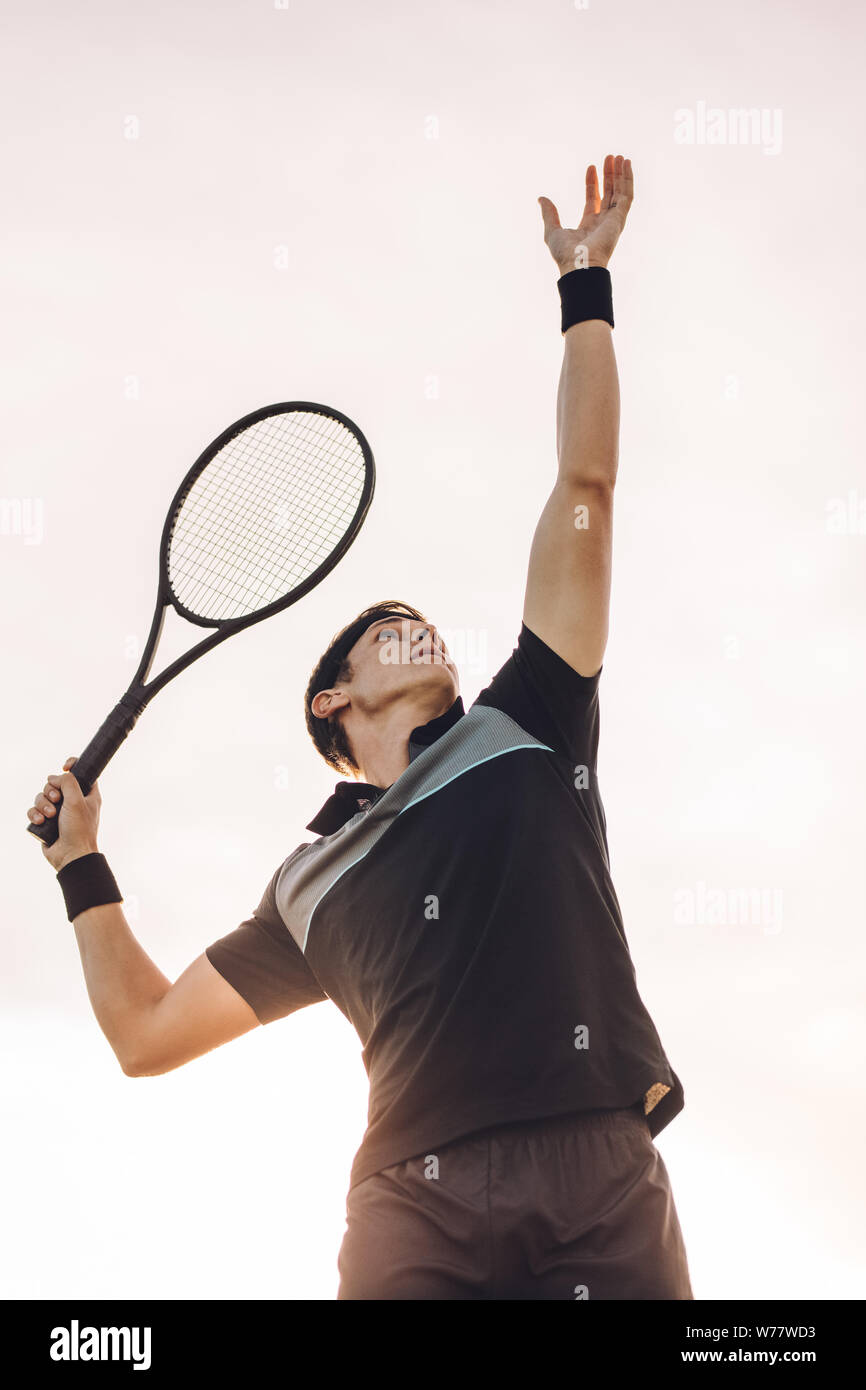 Giocatore di tennis professionista colpendo un servire. Giovane giocatore di tennis in procinto di colpire la palla in una giornata di sole. Foto Stock