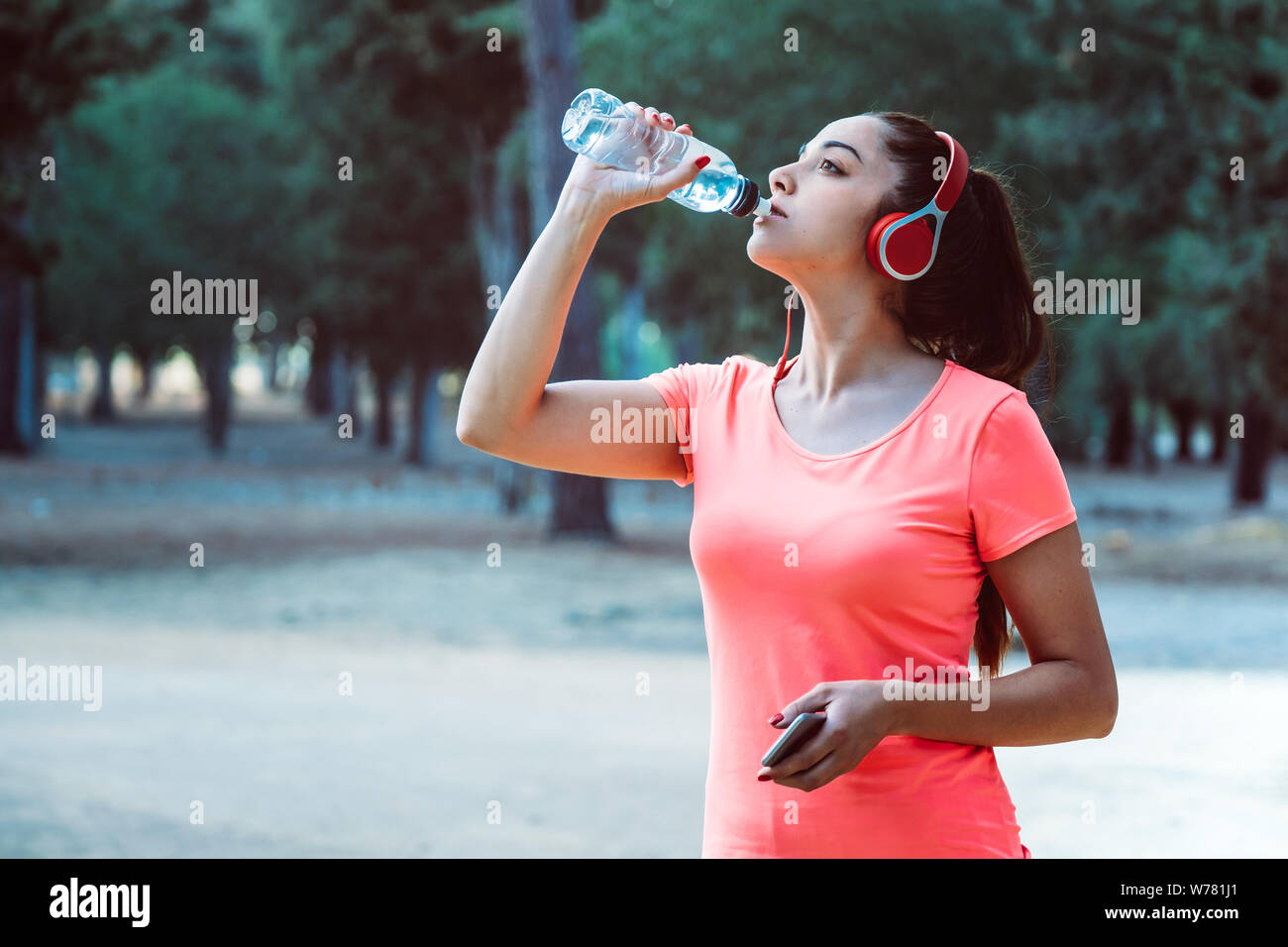 Donna di bere acqua da una bottiglia e ascolta la musica mentre ti alleni Foto Stock