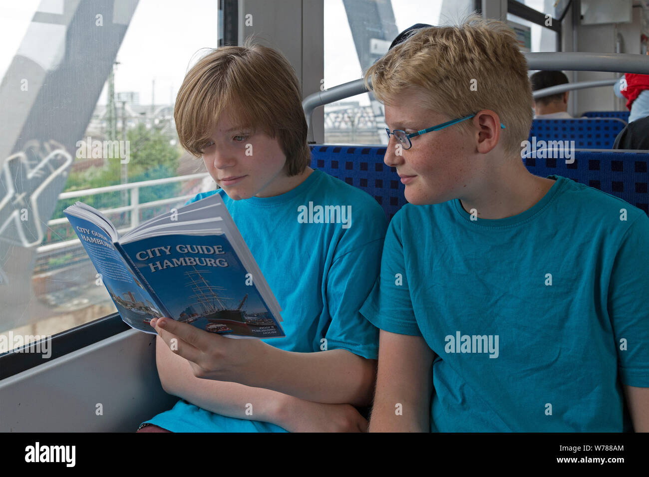 Gli adolescenti durante lo studio della lingua corsa nello studio della loro guida della città su un treno suburbano, Amburgo, Germania Foto Stock