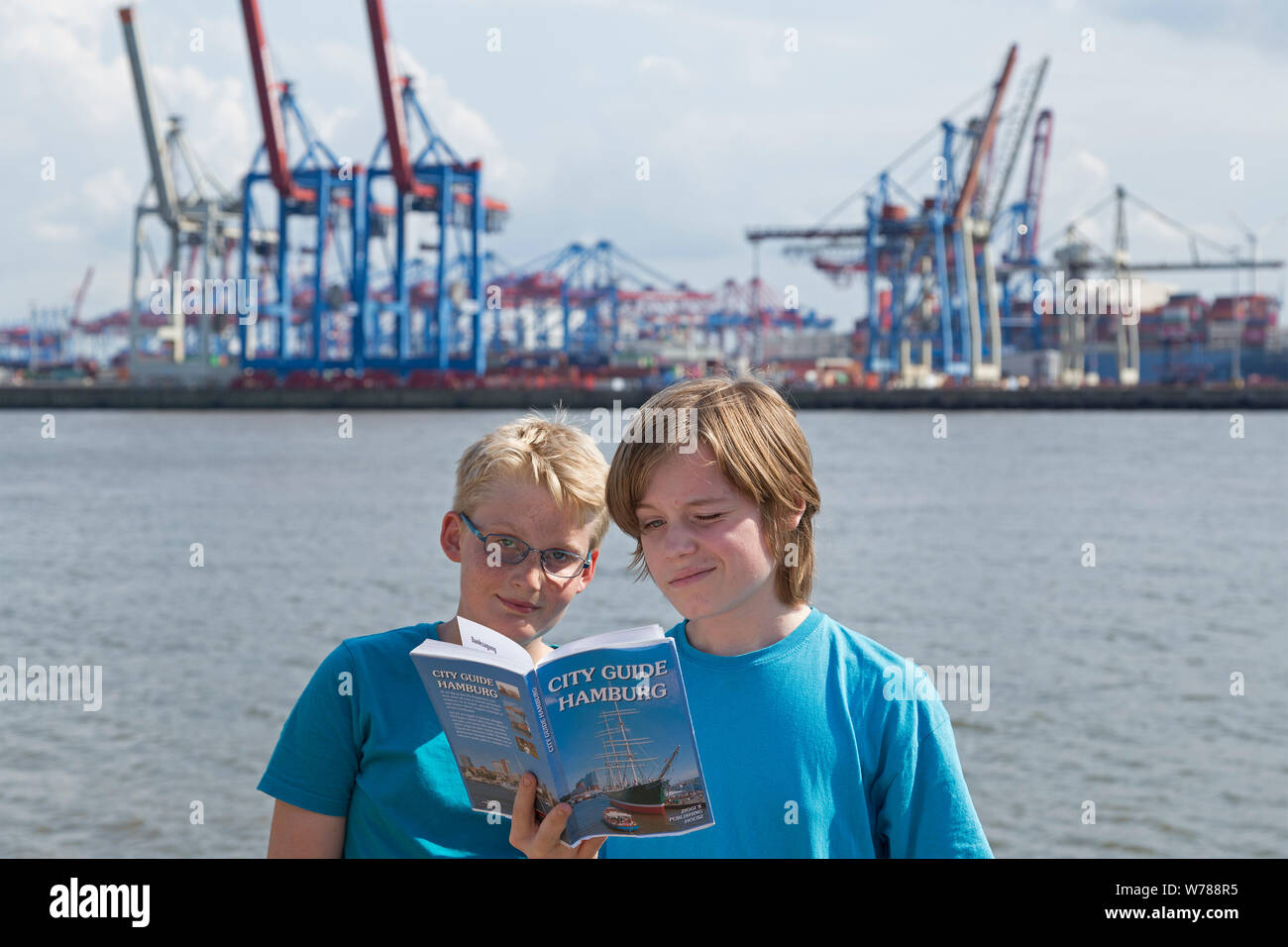 Gli adolescenti durante lo studio della lingua corsa nello studio della loro guida di viaggio accanto al fiume Elba nella parte anteriore del container terminal Burchard-Kai, Amburgo, Germania Foto Stock