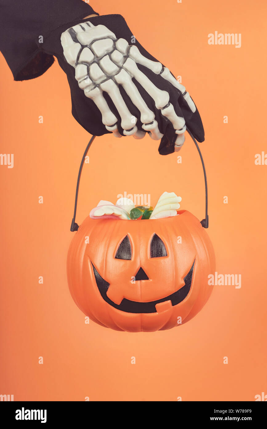 Happy Halloween.del bambino in mano un guanto di scheletro con zucca di Halloween contro lo sfondo arancione Foto Stock