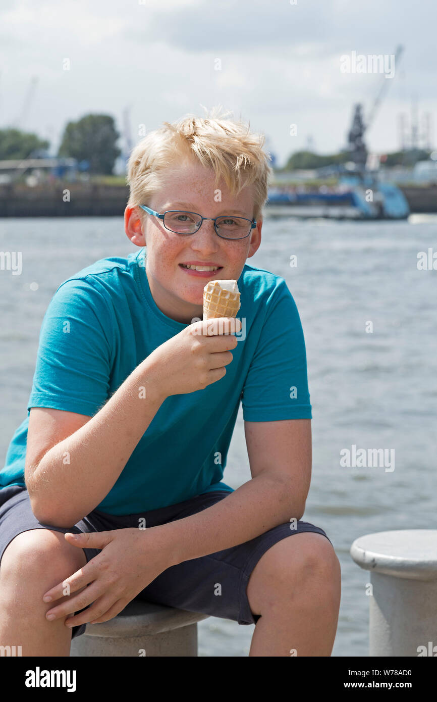 Ragazzo a mangiare il gelato seduto su un bollard su un pontile, Amburgo, Germania Foto Stock