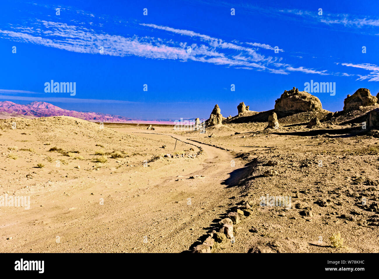 Deserto di strada sterrata che conduce in formazioni rocciose al di là sotto il cielo blu con nuvole bianche. Foto Stock