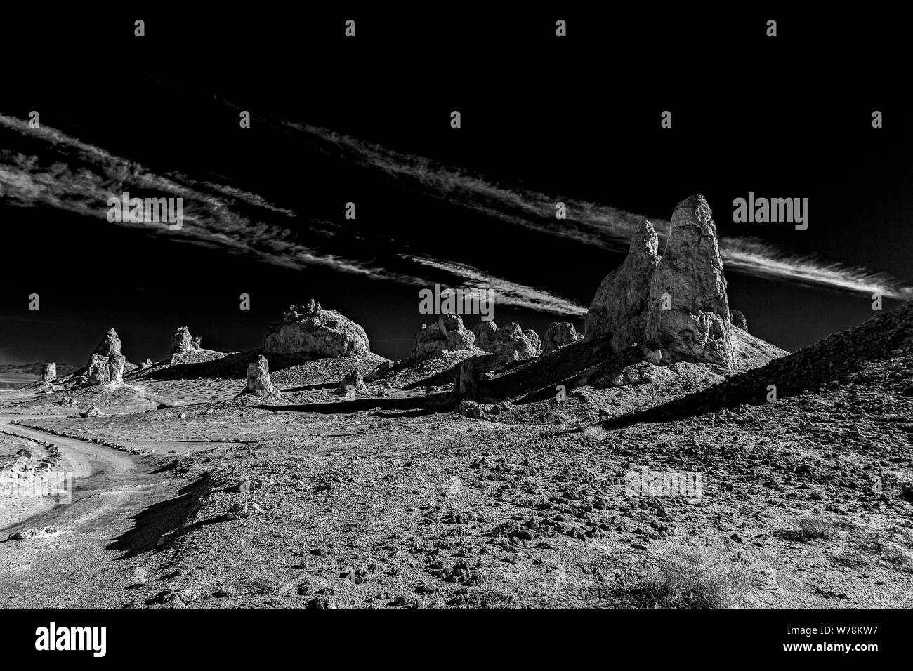 Strada sterrata verso formazioni rocciose e pinnacoli nel deserto scuro sotto cieli neri con nuvole bianche. In bianco e nero. Foto Stock