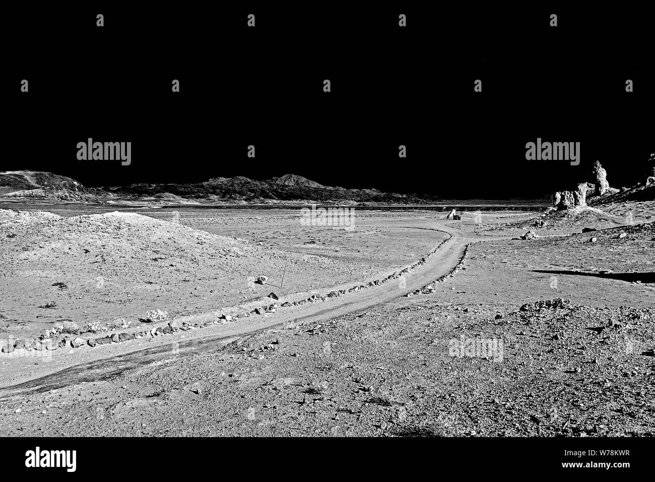 Strada sterrata curvando attraverso il deserto arido valle con le colline e le formazioni rocciose sotto cieli neri. In bianco e nero. Foto Stock