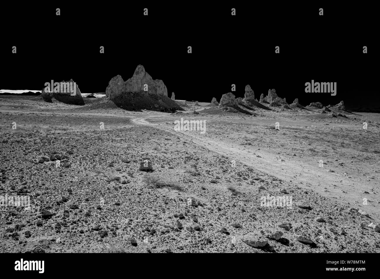 Strada sterrata verso frastagliate formazioni di roccia e pinnacoli sotto cieli neri. Grande vuoto il paesaggio del deserto. Foto Stock