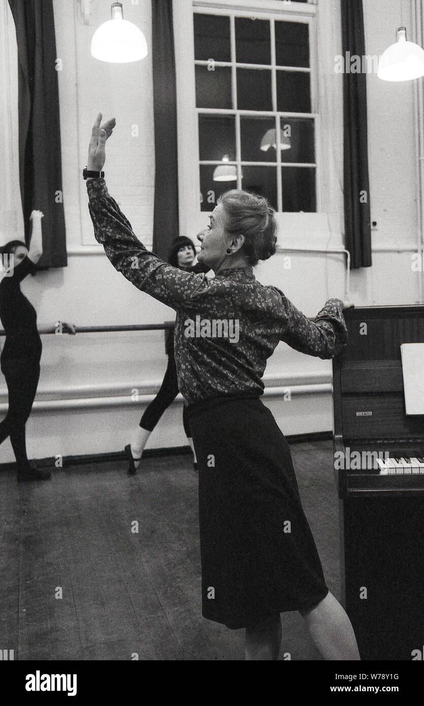 Anni Settanta, in un balletto di interni di classe. una signora anziana insegnante di danza in piedi accanto a un piano indicante la classe come la posa deve cercare e dove il braccio dovrebbe essere posizionato. Un balletto o lezioni di danza sono state un tradizionale e popolare modo di migliorare la postura e la flessibilità. Foto Stock