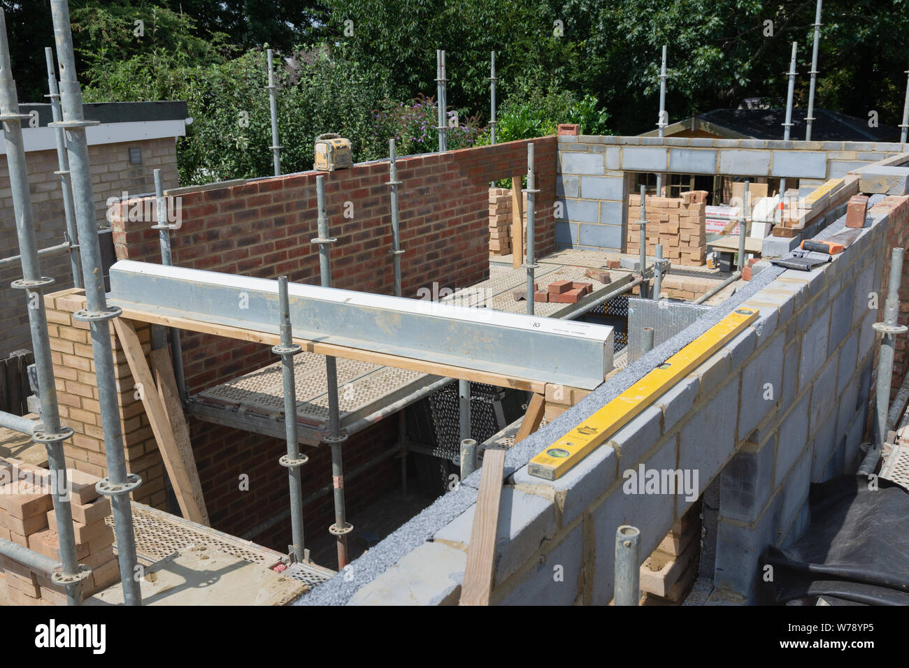 Progetti di ristrutturazione. Costruzione di estensione della casa esistente, incompiuto di pareti in mattoni, blocco funzionano, isolamento, pile di materiali su scaffoliding, Foto Stock