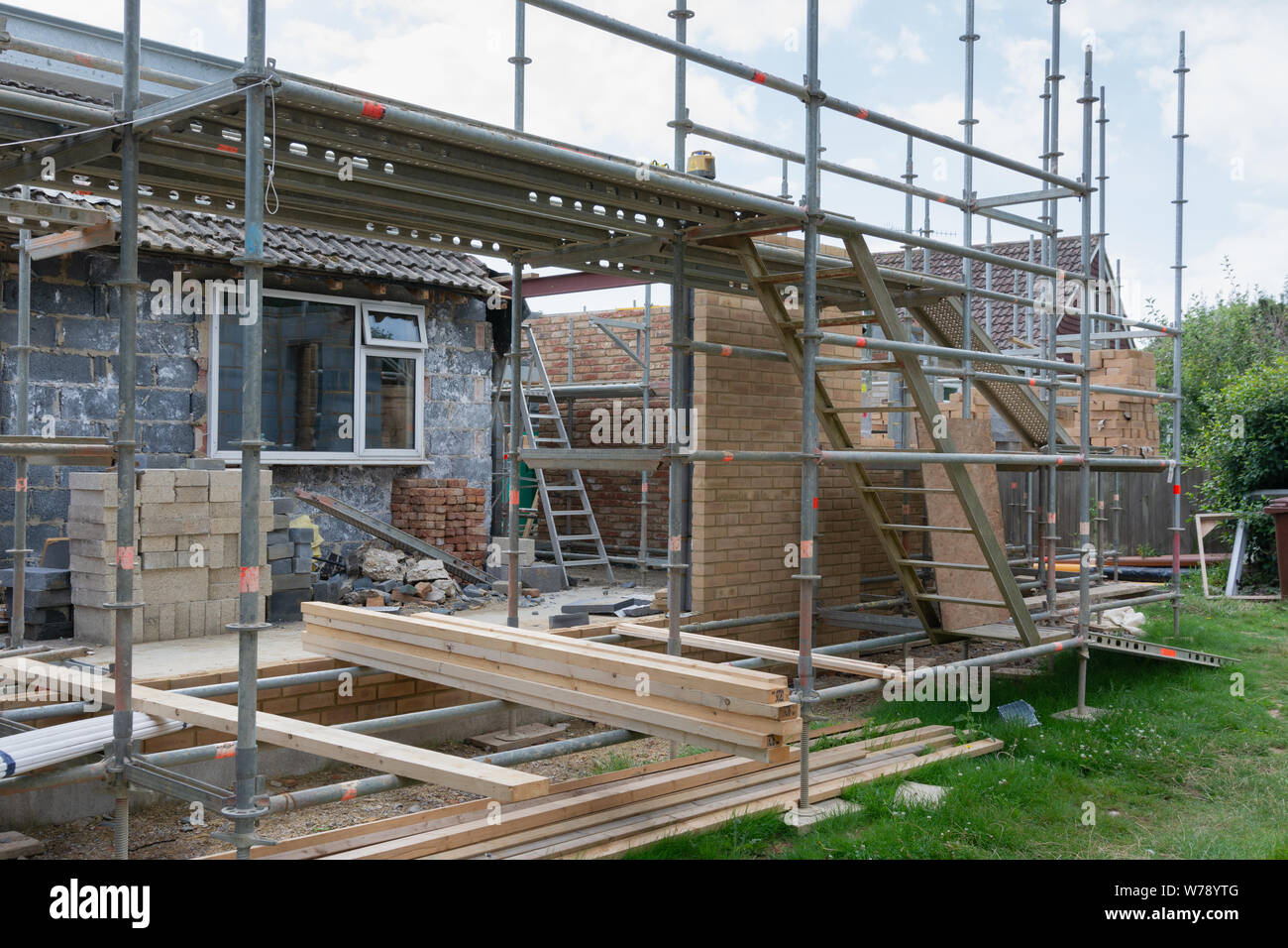 Progetti di ristrutturazione. Costruzione di estensione della casa esistente, incompiuto di pareti in mattoni, blocco funzionano, isolamento, pile di materiali su scaffoliding, Foto Stock