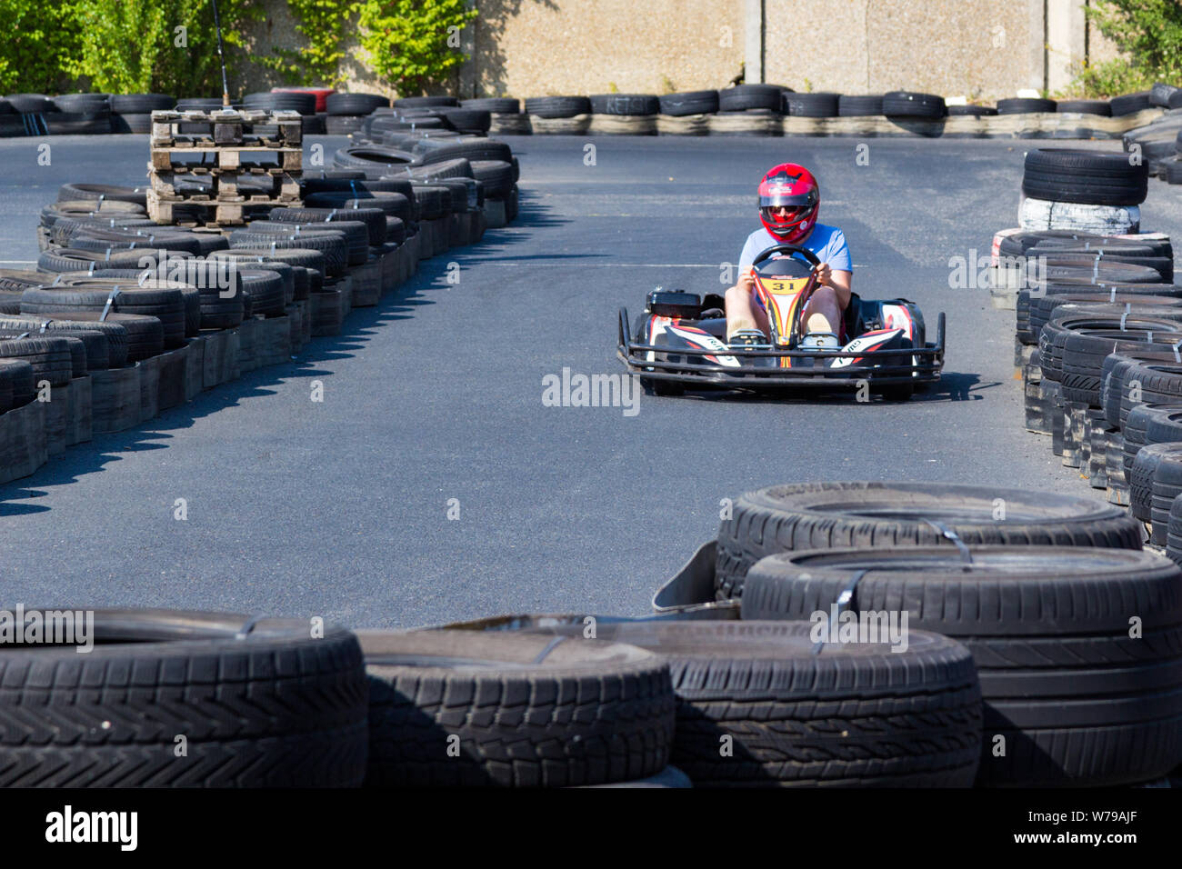 Go-kart in rosso casco racing tra sicurezza barriere di pneumatici, vista frontale Foto Stock