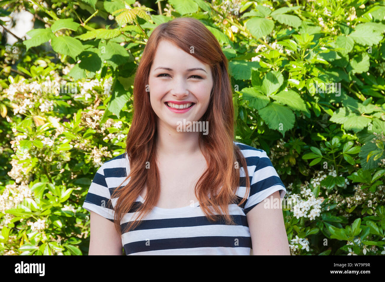 Una giovane donna con i capelli rossi sorridente alla fotocamera. Foto Stock