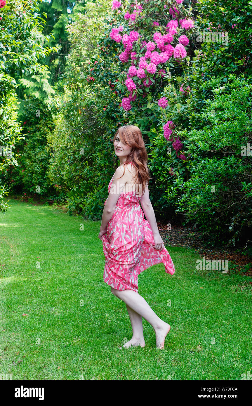 Giovane donna con i capelli rossi a camminare a piedi nudi sull'erba verde in primavera. Foto Stock