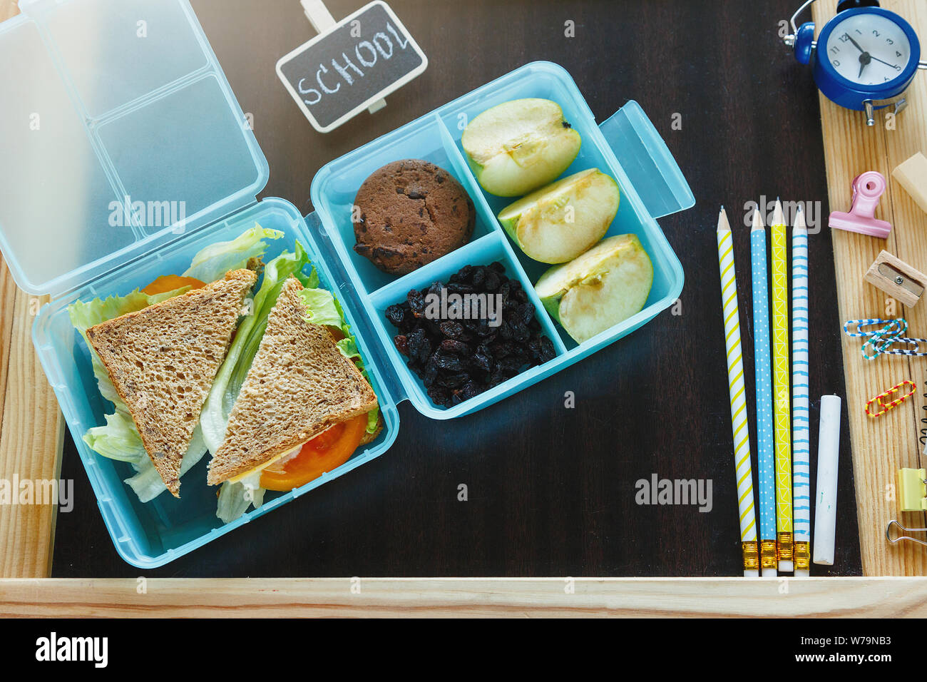 Scuola blue scatola di pranzo con sandwich fatti in casa, mela verde, cookie, matite, orologio, notebook sul tavolo. Mangiare sano a scuola. Si torna a scuola Foto Stock