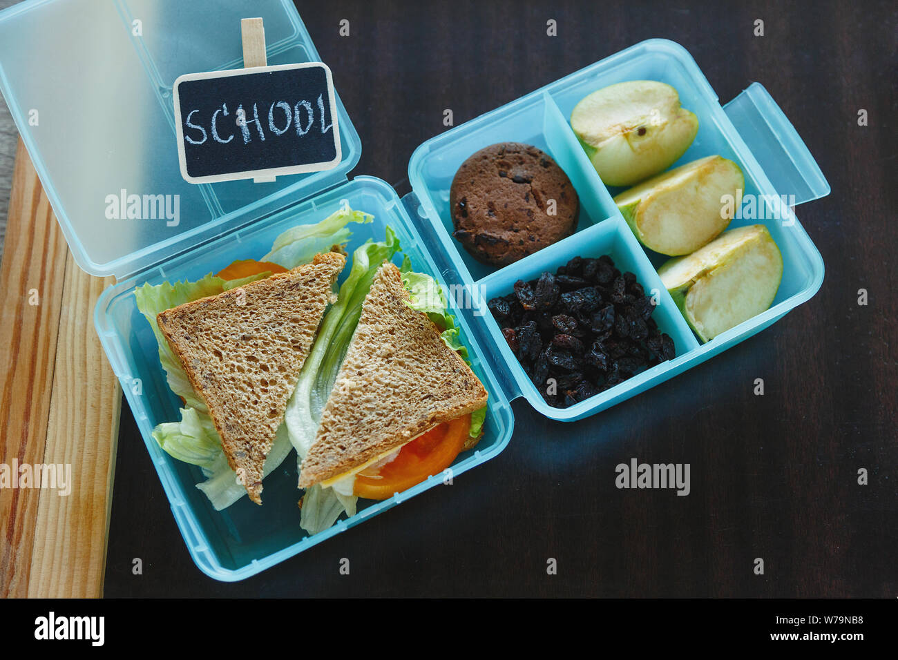 Scuola blue scatola di pranzo con sandwich fatti in casa, mela verde, cookie, matite, orologio, notebook sul tavolo. Mangiare sano a scuola. Si torna a scuola Foto Stock