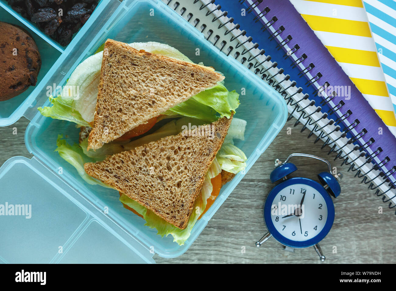 Scuola blue scatola di pranzo con sandwich fatti in casa, mela verde, cookie, matite, orologio, notebook sul tavolo. Mangiare sano a scuola. Si torna a scuola Foto Stock