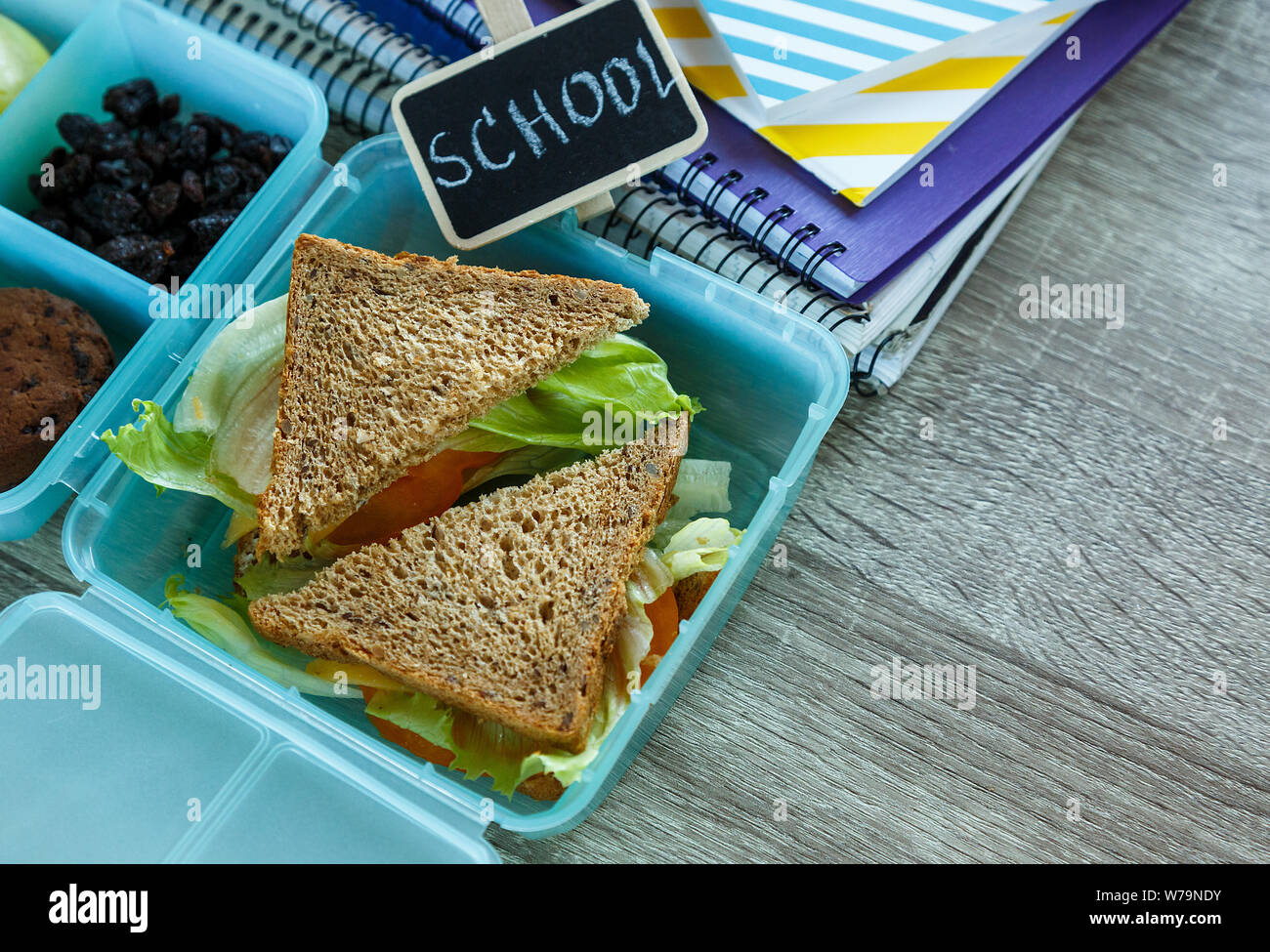 Scuola blue scatola di pranzo con sandwich fatti in casa, mela verde, cookie, matite, orologio, notebook sul tavolo. Mangiare sano a scuola. Si torna a scuola Foto Stock
