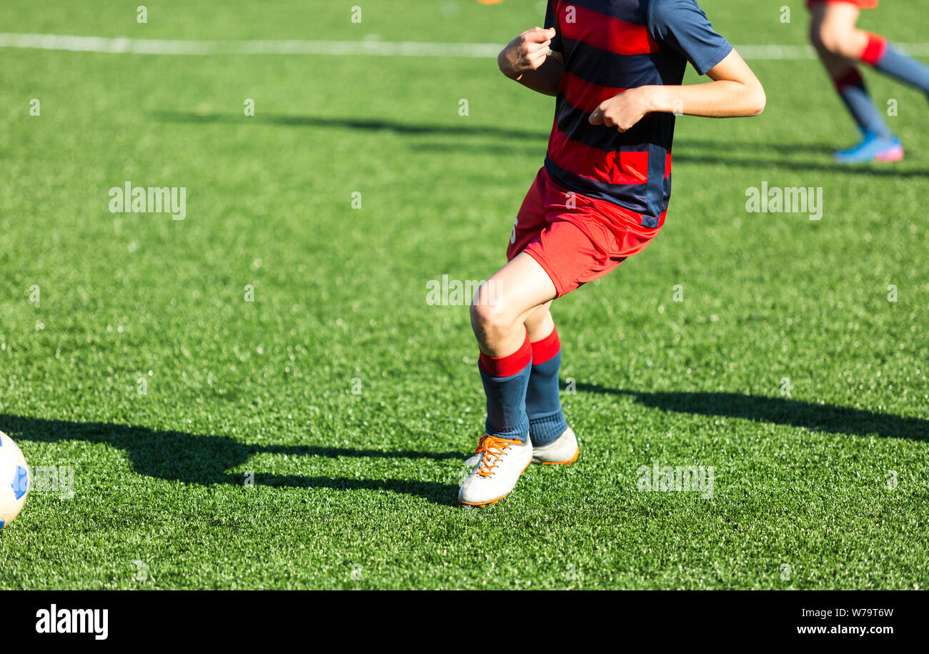 I ragazzi in rosso e blu per abbigliamento sportivo gioca a calcio sul campo, dribbling palla. I giovani giocatori di calcio con la palla sul prato verde. Formazione, calcio Foto Stock