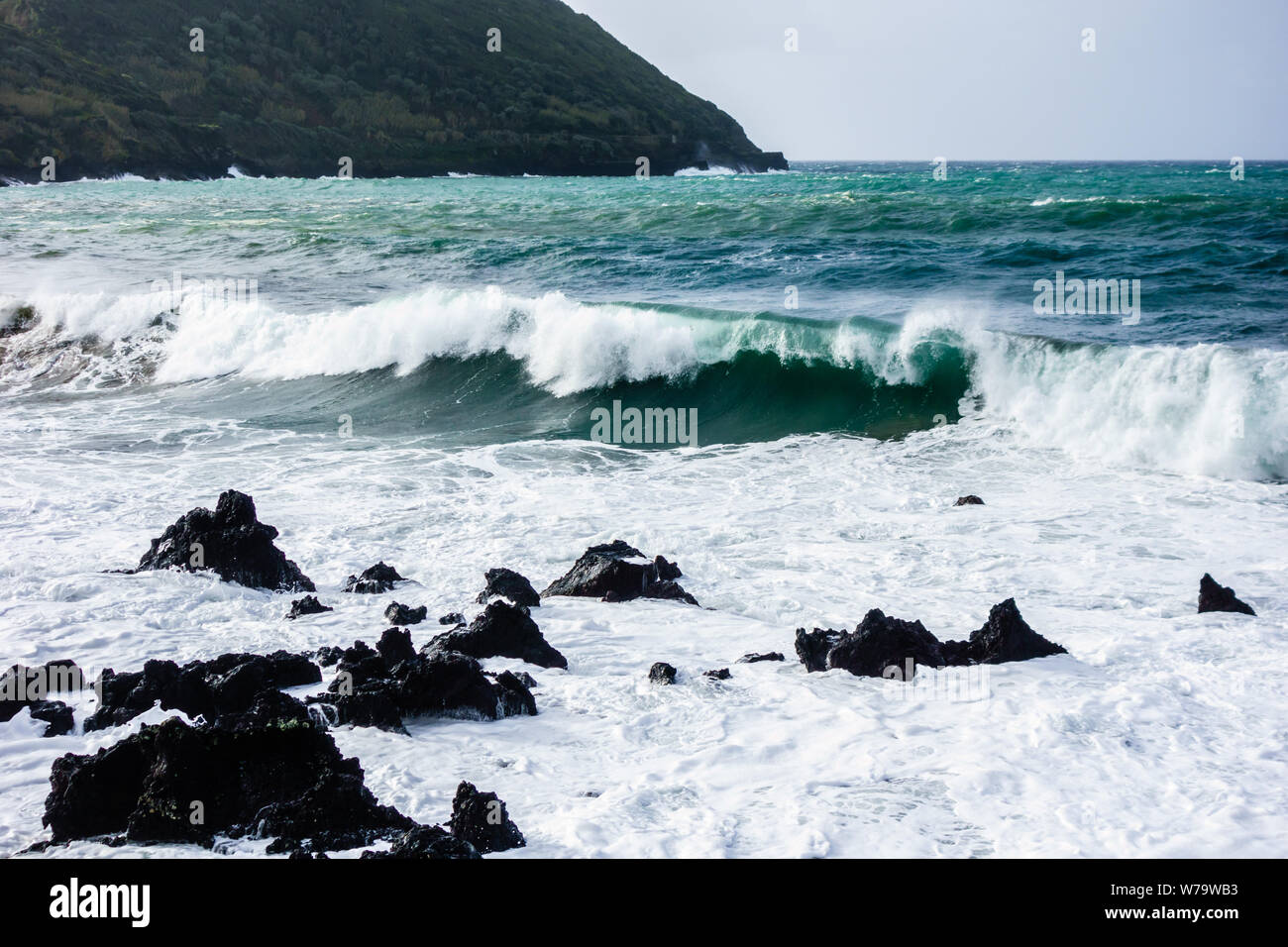 Potente oceano onde che si infrangono sulle frastagliate rocce di basalto con isola in background, nelle Azzorre, Portogallo. Foto Stock