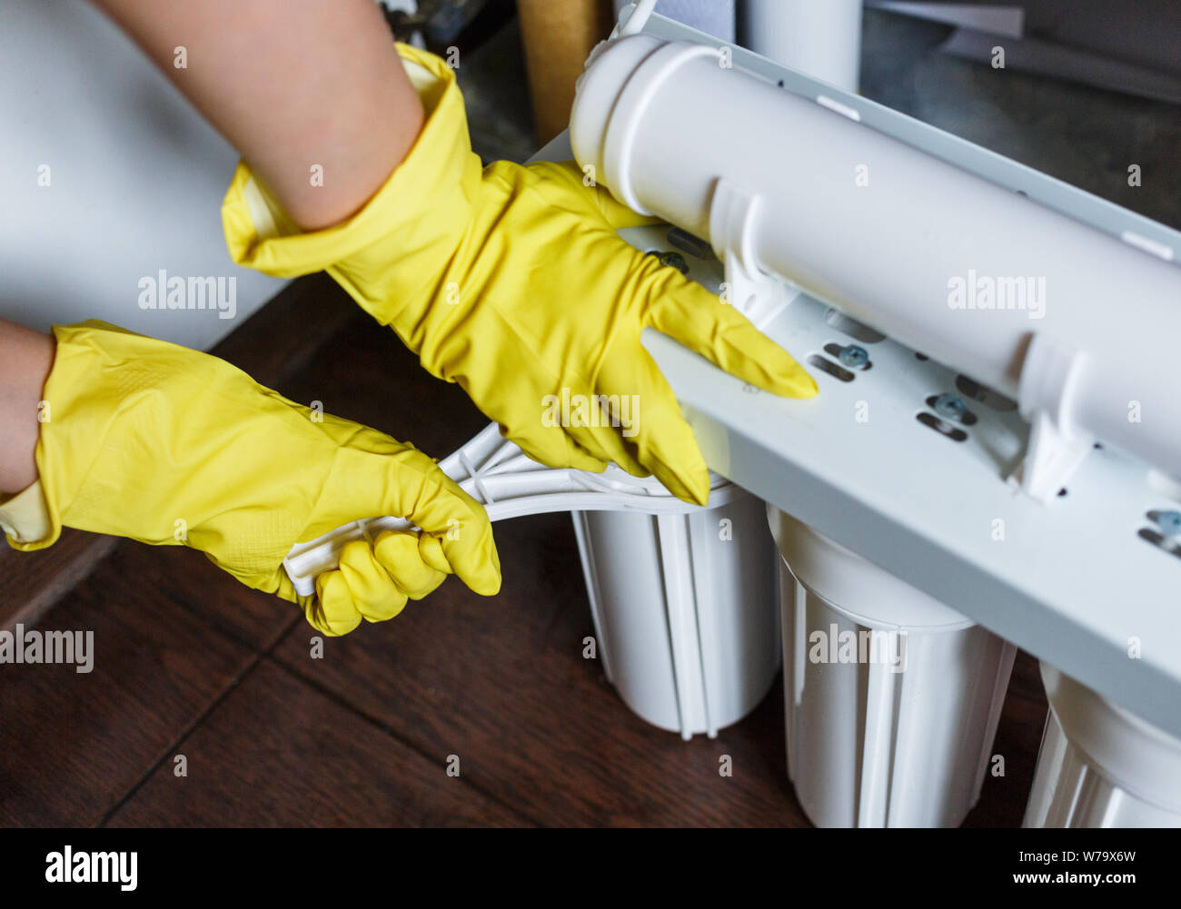 Plumber in giallo guanti per la casa cambia filtri per l'acqua. Repairman installazione di acqua le cartucce del filtro in cucina. Acqua potabile sistema di filtrazione i Foto Stock