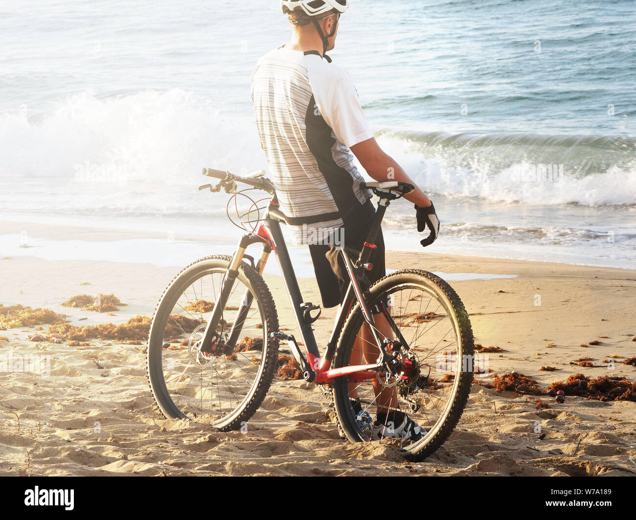 Ciclista in appoggio sulla spiaggia dell'Oceano Atlantico. Vista posteriore. Tramonto. sun flare. Foto Stock