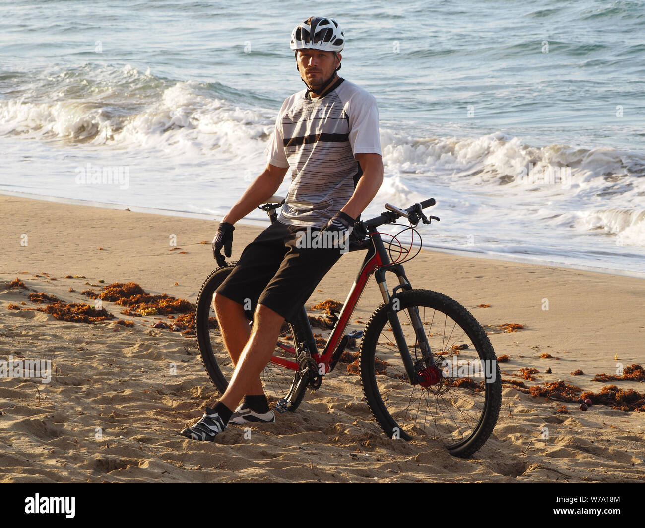 Uomo con una bicicletta in appoggio sulla spiaggia Foto Stock