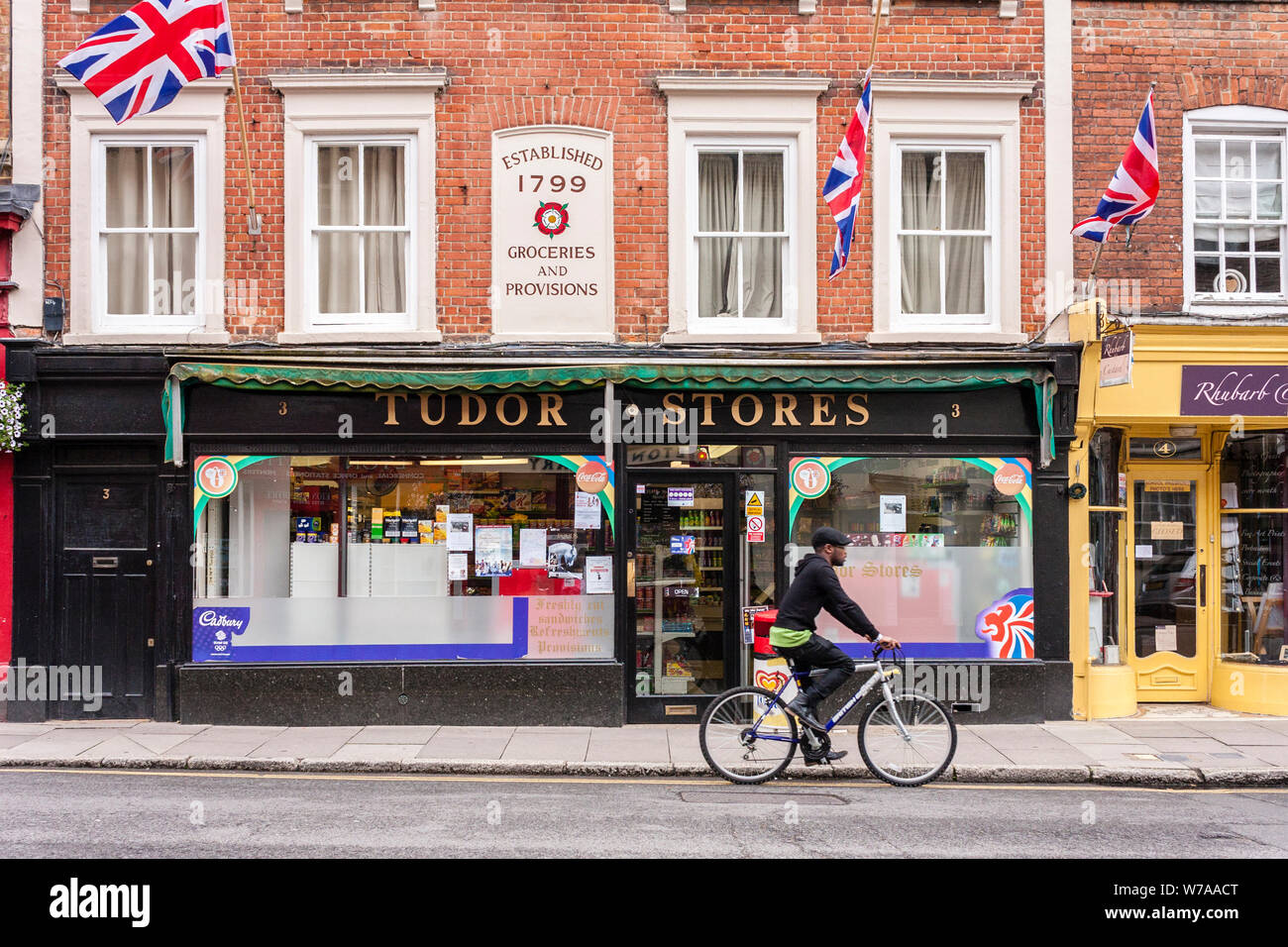 Ciclista passa un negozio locale di negozio a Eton High Street, Berkshire, Inghilterra, GB, Regno Unito Foto Stock